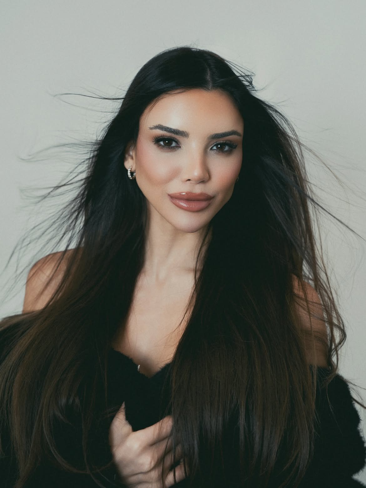 Eileen León with long dark hair blown by the wind, in a black faux-fur coat