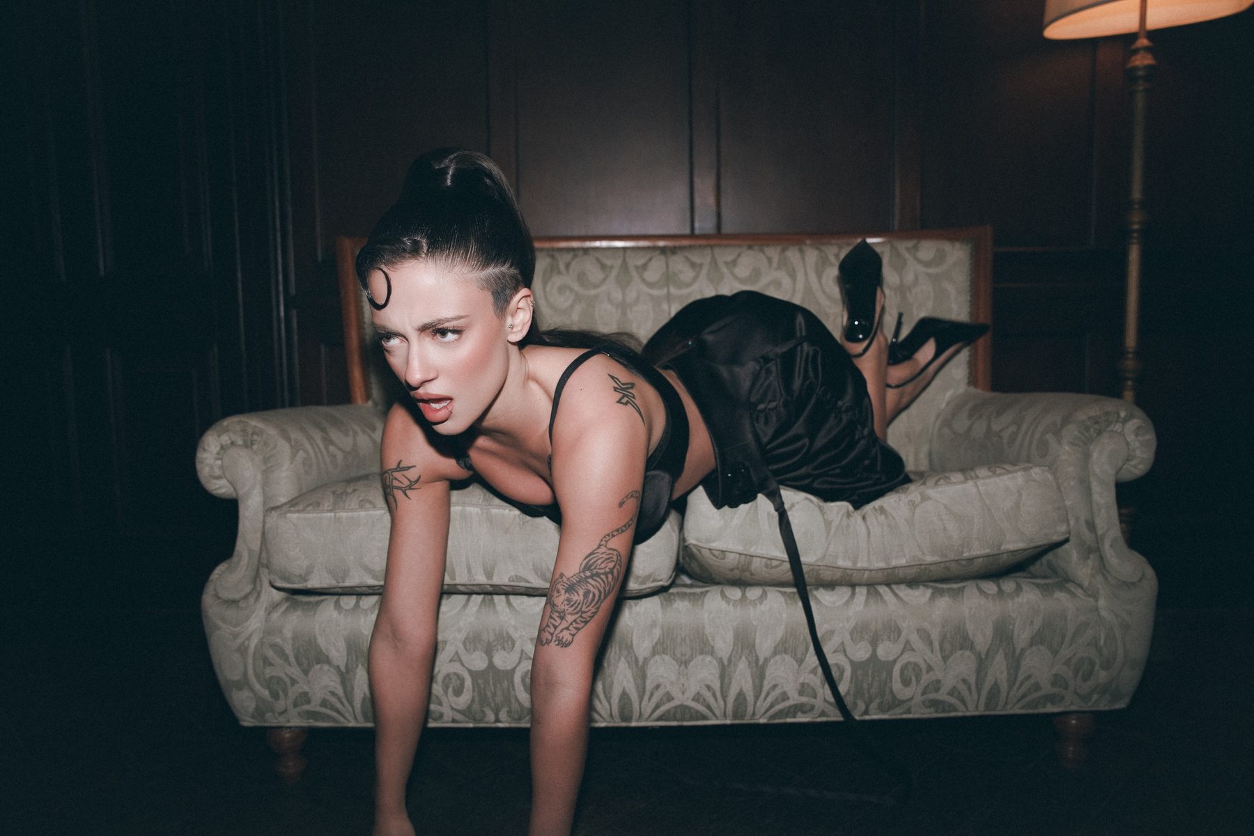 Greta Cozzolino leaning off a damask sofa toward the camera, direct flash