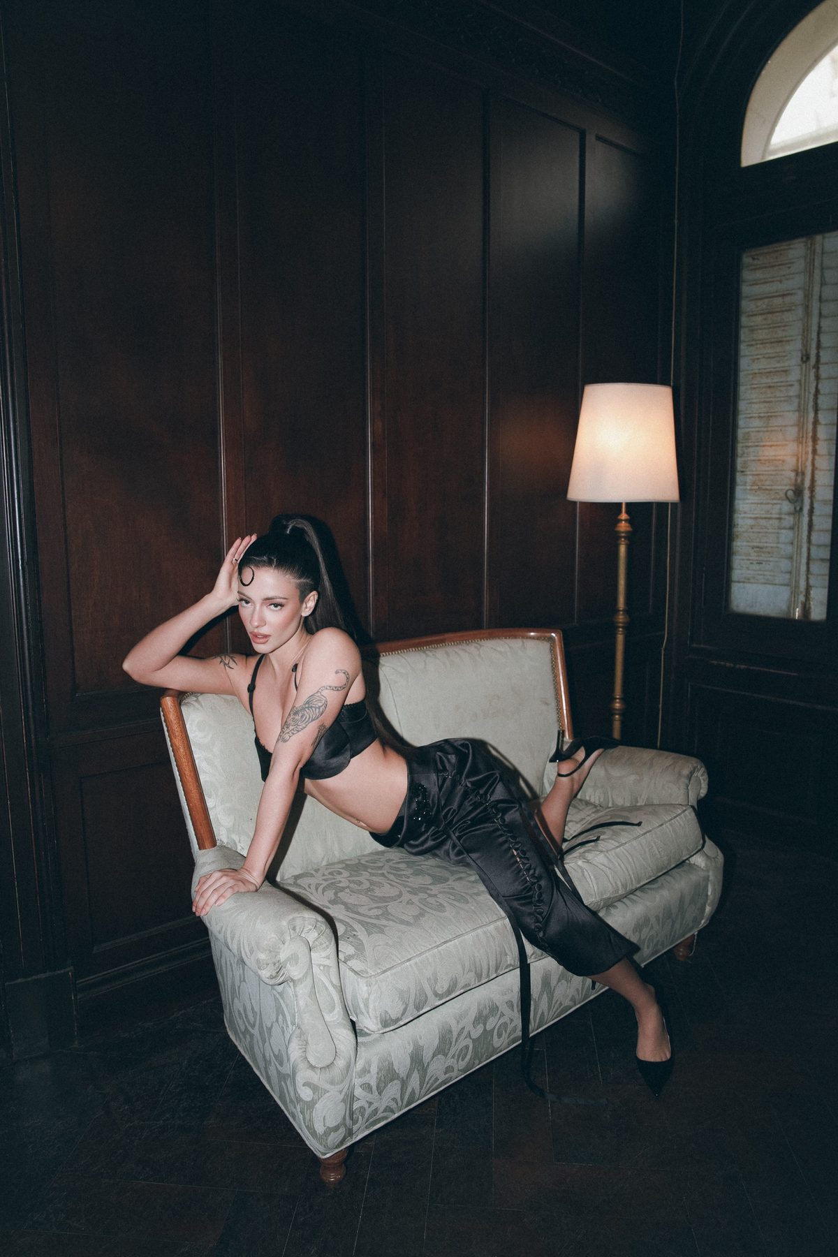 Greta Cozzolino reclining on a damask sofa beside a floor lamp