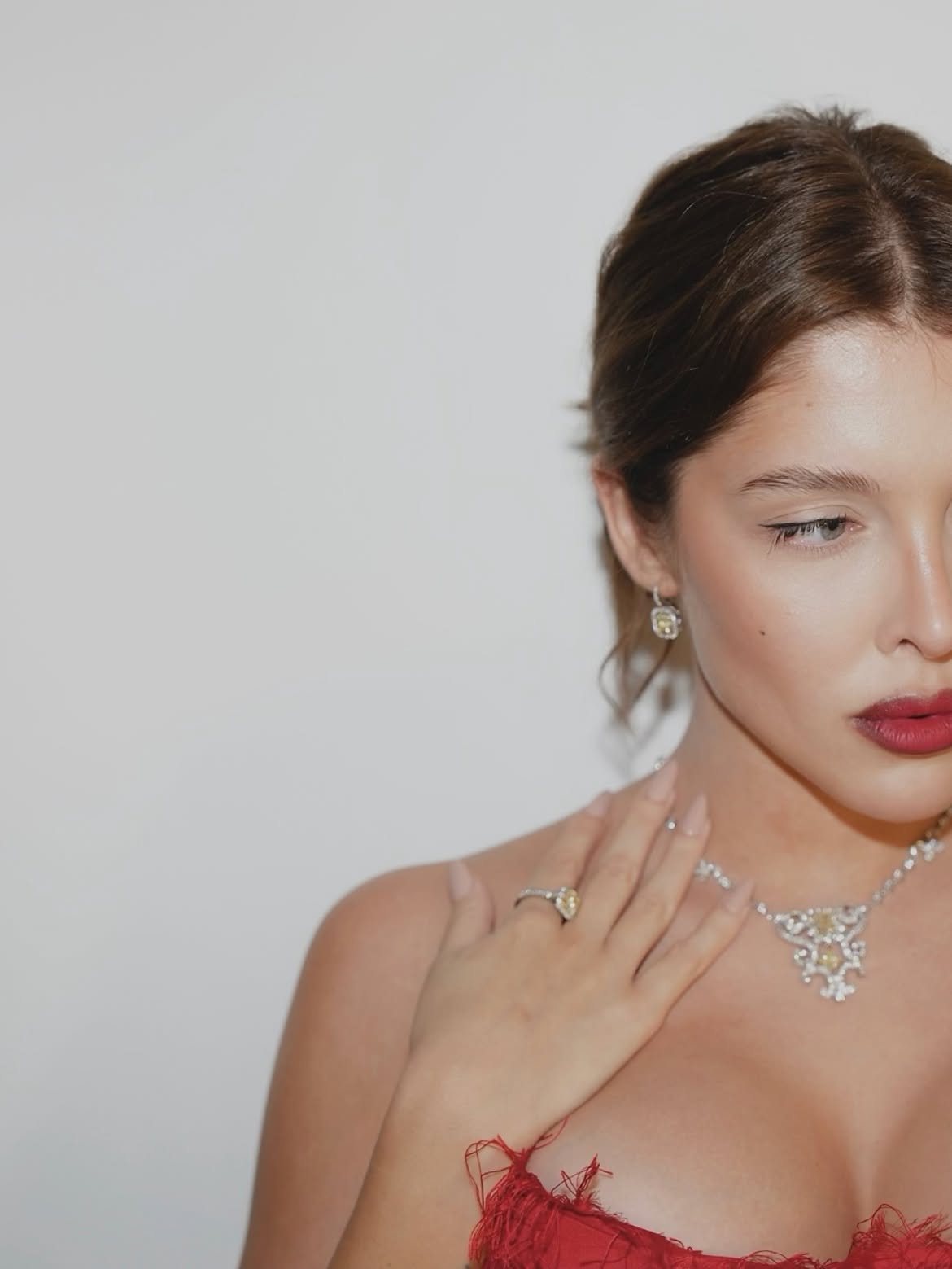 Close portrait of Sofía Gonet with red lips and a diamond necklace against a white wall