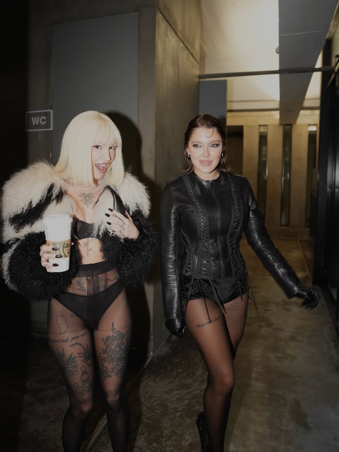 La Joaqui and Sofía Gonet walking past the WC sign, direct flash