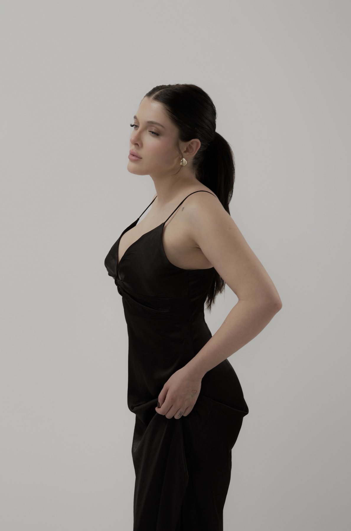 Sofía Gonet in profile in a black satin slip dress, holding the skirt