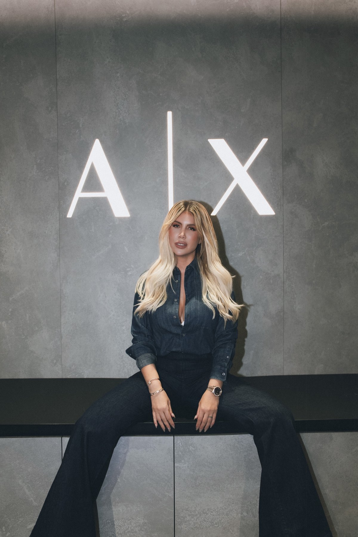 Wanda Nara seated in denim beneath the backlit A|X logo